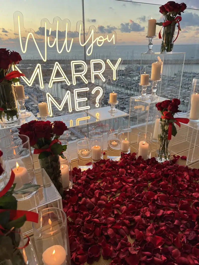 שלט ניאון Will You Marry Me מקרוב, בין ורדים אדומים ונרות