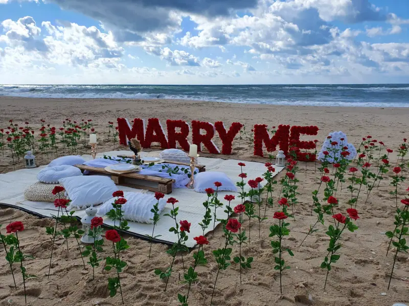 אותיות MARRY ME אדומות ופיקניק נמוך על החוף, באור יום