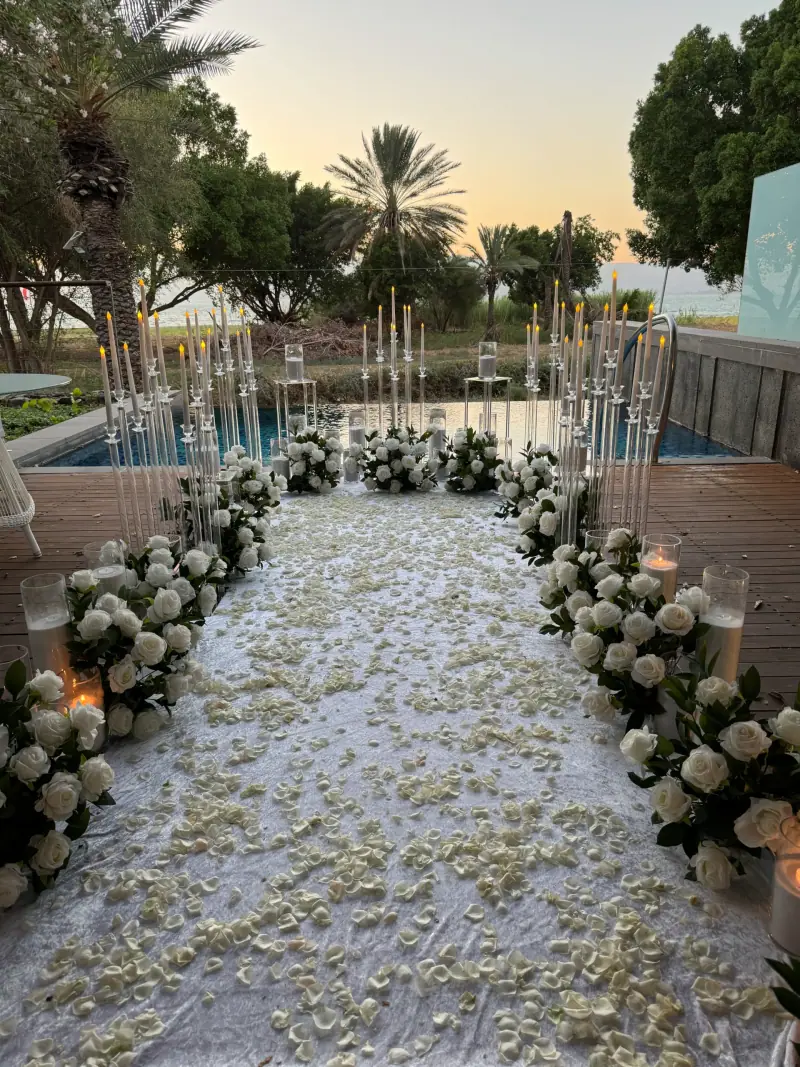 שביל לבן בין סידורי פרחים ונרות גבוהים ליד בריכה