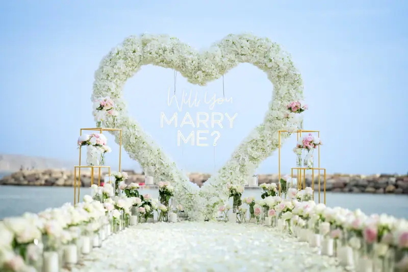 לב פרחים לבן עם שלט Will You Marry Me ומעמדים מוזהבים באור יום