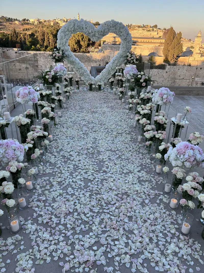 לב פרחים לבן בקצה שביל ארוך של עלי כותרת לבנים, עם סידורי פרחים לבנים גבוהים משני הצדדים